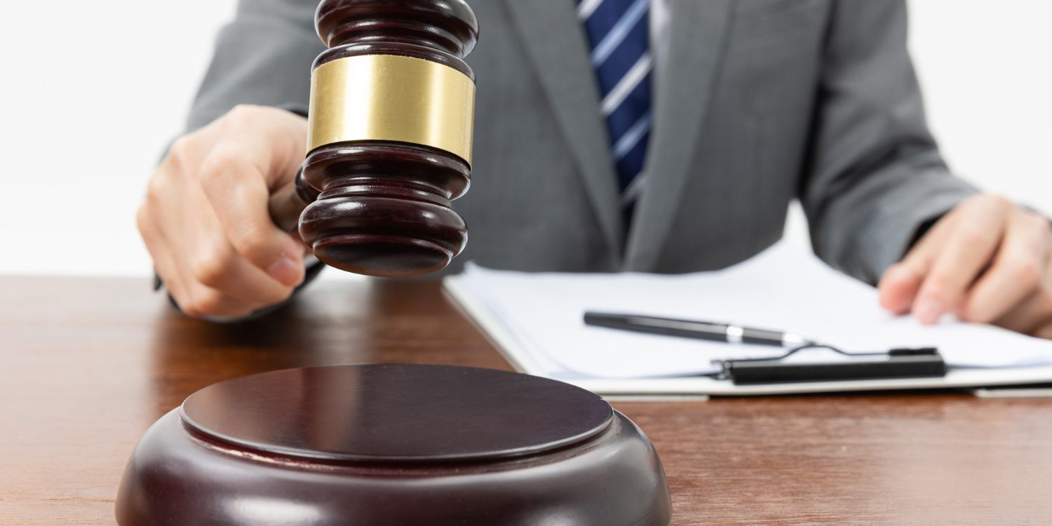 closeup-shot-person-with-gavel-hand-papers-table