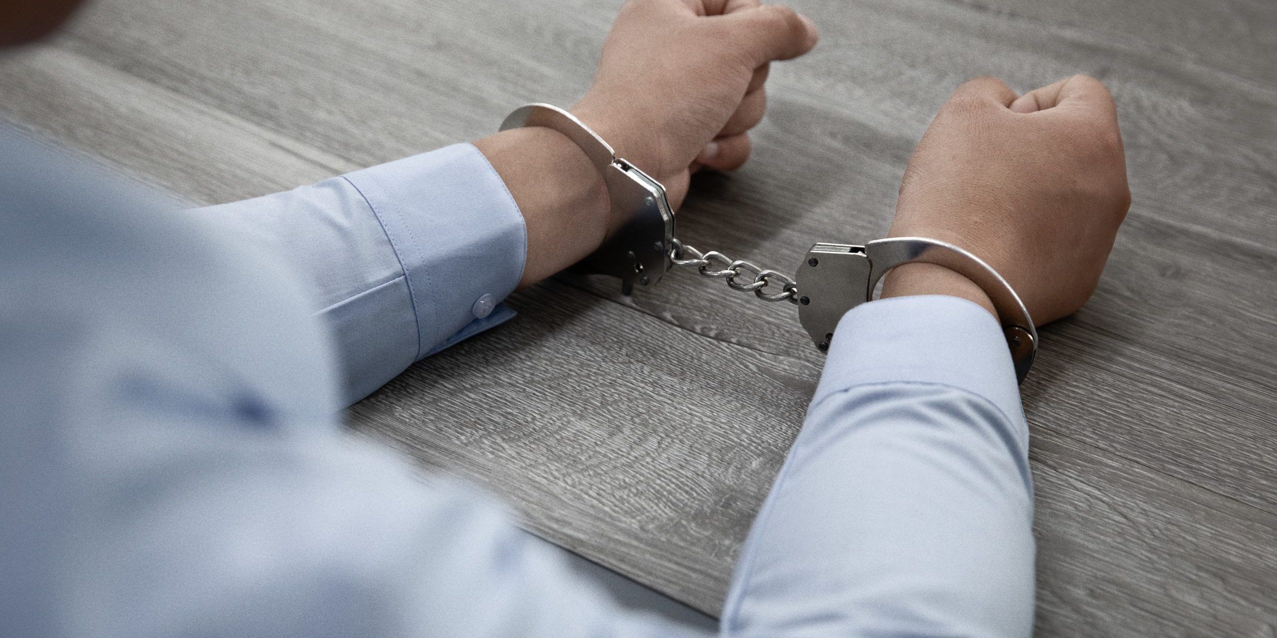 Selective focus shot of male hands in handcuffs on a wooden table